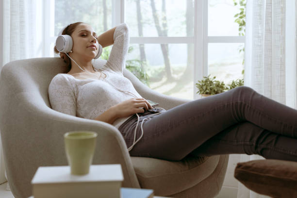 serein détendu femme reposant sur le fauteuil à la maison, elle est à l’écoute de la musique avec les yeux fermés - armchair comfortable relaxation headphones photos et images de collection
