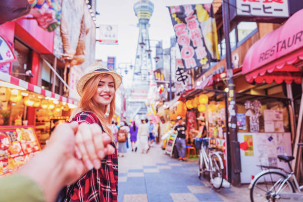 Holding Hands and Exploring Famous Streets of Shinsekai, Osaka, Japan Travel, Tourism, Vacation, Relationship - Young attractive cheerful female holding boyfriend’s hand and exploring the famous market streets of Shinsekai, in Osaka, Japan. osaka prefecture stock pictures, royalty-free photos & images