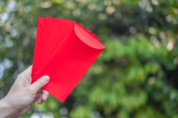 Happy Chinese new year, Hand holding red envelope or called Angpao isolated on green bokeh background from trees. stock photo