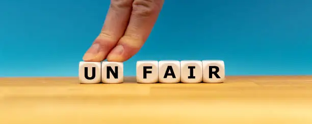 Dice form the word "UNFAIR" while two fingers push the letters "UN" away in order to change the word to "FAIR".