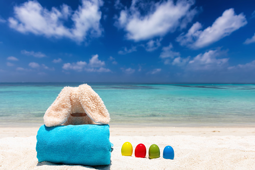 Easter vacation travel concept: relaxed easter bunny with colourful easter eggs on a tropical beach