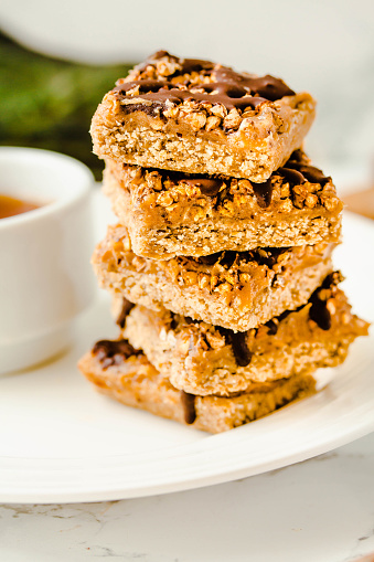istock Granola bar with date caramel and chocolate. Healthy sweet dessert snack. Cereal granola bar with nuts, fruit and berries on a white marble table. A cup of coffee.Healthy breakfast. 1125868210