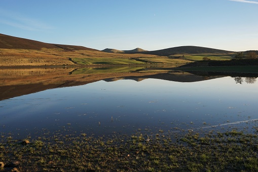 Pentland Hills, Edinburgh, Scotland - 14 October 2018: A sunny autumn afternoon with a flat calm on the surface of Threipmuir reservoir, near Edinburgh. The hills on the far side are reflected on the smooth surface of the water.