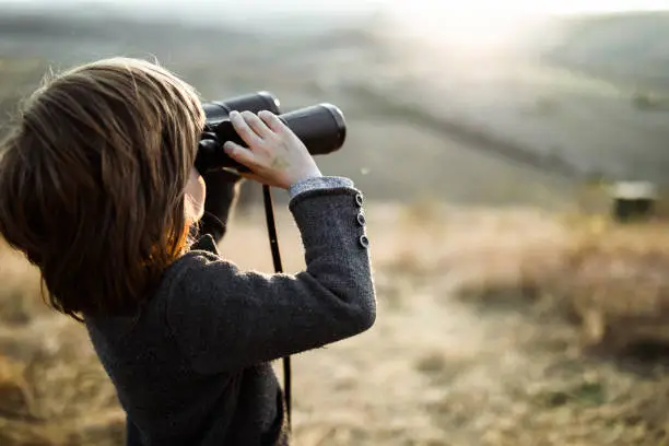 Little kid using binoculars while looking at view in autumn day. Copy space.