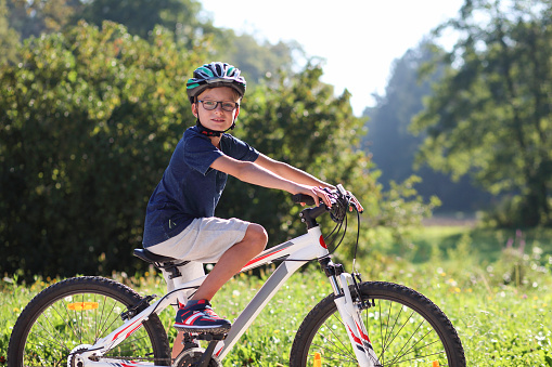 Boy with cycling helmet sitting on his bike taking a break, looking at camera, riding through nature.