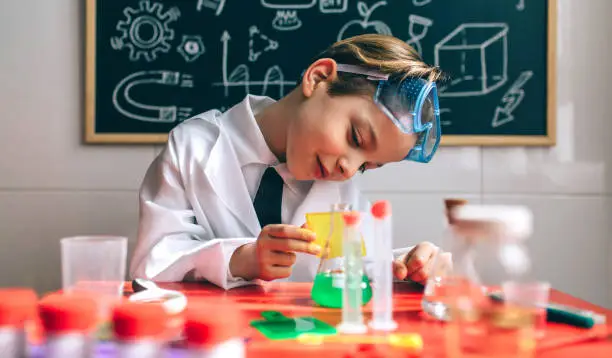 Boy dressed as chemist playing with chemistry game in front of a blackboard with drawings