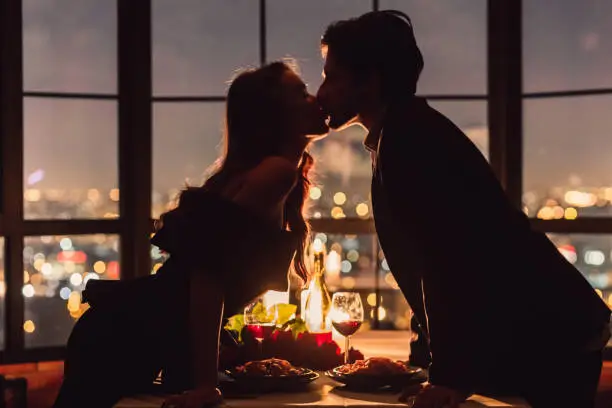 Loving couple kissing on panoramic window background overlooking nigth city. Romantic place for romantic evening concept