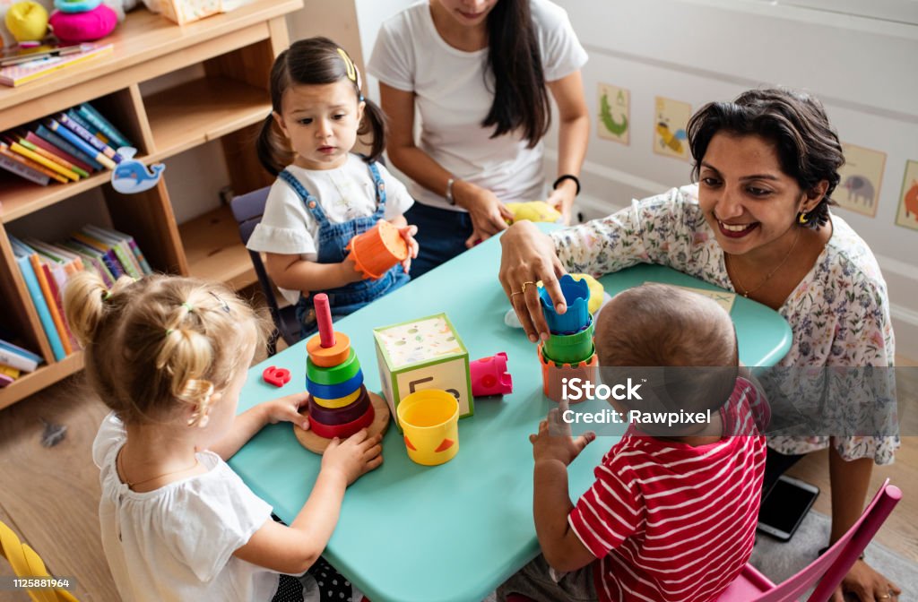 Bambini in asilo che giocano con l'insegnante in classe - Foto stock royalty-free di Servizi per l'infanzia