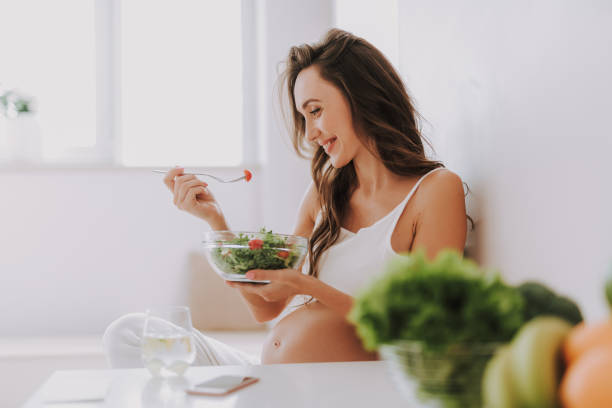 istock Attractive mom holding fork with tomatoes and eating fresh salad on kitchen 1125882013
