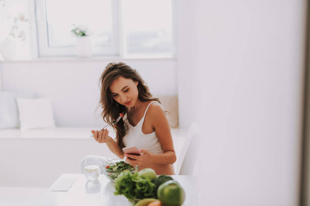 istock Young woman looking at cellular and tasting salad 1125882028
