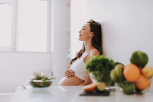 calm expectant mama sitting on chair and holding hands on stomach - eating female healthcare and medicine healthy lifestyle imagens e fotografias de stock