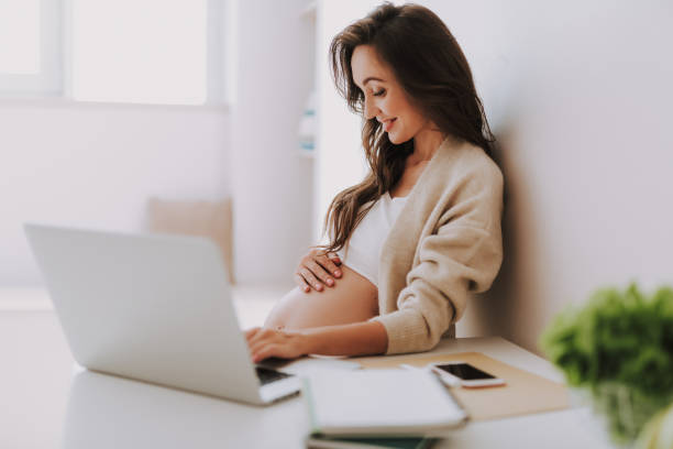 istock Attractive future mama smiling and sitting behind pc laptop in room 1125882045