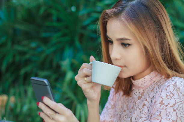 istock Young Woman Using Mobile Phone While Drinking Coffee Against Plants 1125886300