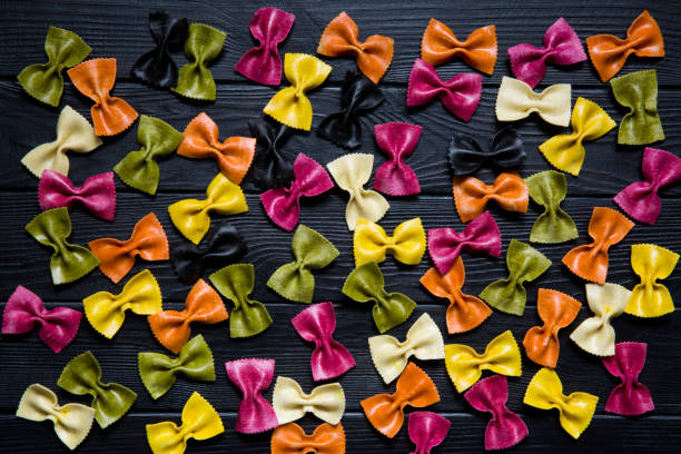 Assortment of colorful farfalle or farfalline on wooden rustic black background. Italian cuisine. Pink, green, red, purple, yellow and orange.