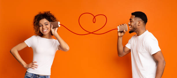 Young black couple with can phone on orange background Communication and fun. Young black couple talking through tin can phone, orange background, panorama string telephone stock pictures, royalty-free photos & images