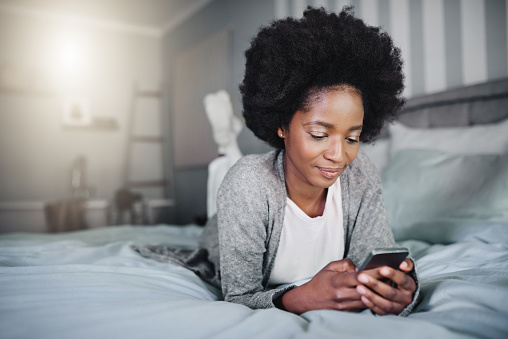 Shot of a young woman using a mobile phone in her bed at home