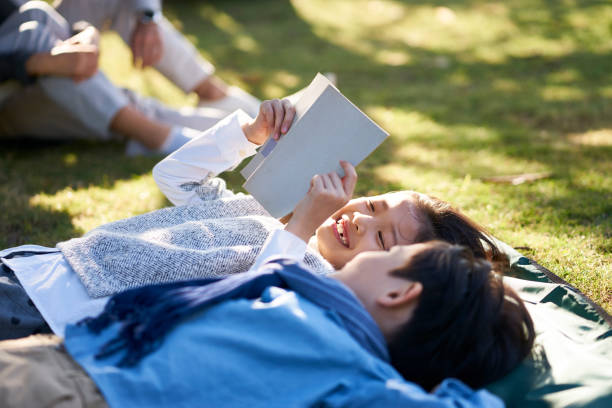 istock two asian children lying on back on grass reading book 1125905145