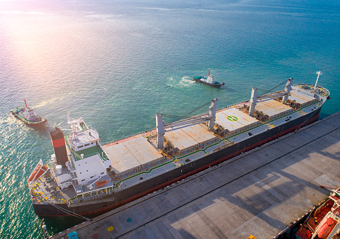 aerial view of general bulk cargo ship vessel on departure unberthing from the sea port terminal, safety circumstance sailingh by tug boats assist pull towage under navigation command pilot