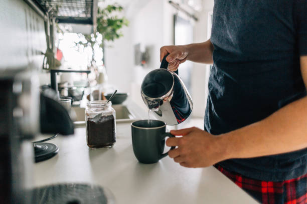 Preparing first cup of coffee in the morning Young man preparing first cup of coffee in the morning in the kitchen of his apartment coffee maker stock pictures, royalty-free photos & images