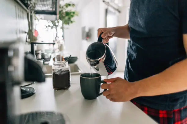 Young man preparing first cup of coffee in the morning in the kitchen of his apartment