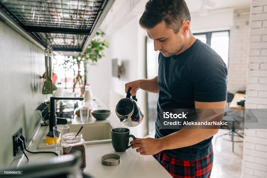 Preparing first cup of coffee in the morning Young man preparing first cup of coffee in the morning in the kitchen of his apartment Kitchen Stock Photo