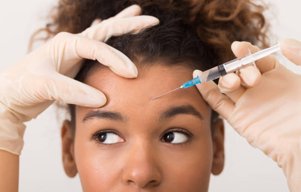 African-american woman getting botox injection in forehead Cosmetic procedures. African-american woman getting botox injection in forehead needle plant part photos stock pictures, royalty-free photos & images