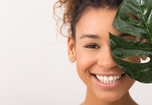 African-american woman with fresh leaf covering half of face on white background with copy space