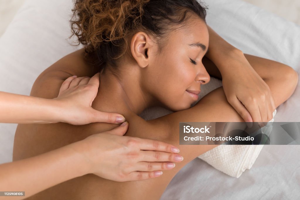 African-american woman enjoying shoulder massage in spa African-american woman enjoying shoulder massage, lying with closed eyes in spa center Massaging Stock Photo