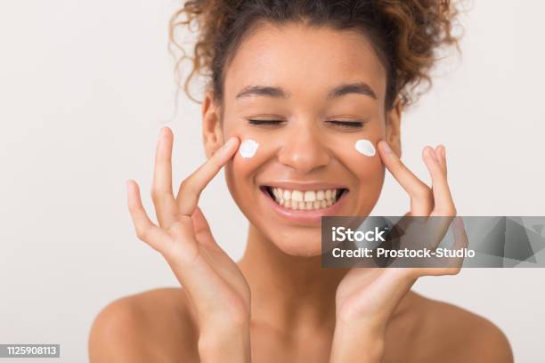 Laughing Girl Applying Moisturizing Cream On Her Face Stock Photo - Download Image Now