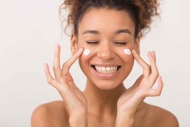 laughing girl applying moisturizing cream on her face - moisturizer cosmetics merchandise human hand imagens e fotografias de stock