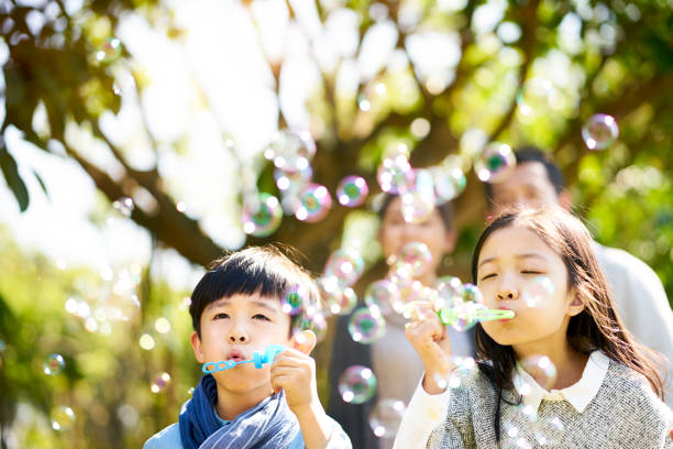 petit garçon asiatique et fillette avec amusement soufflant des bulles - bubble wand child outdoors bubble photos et images de collection