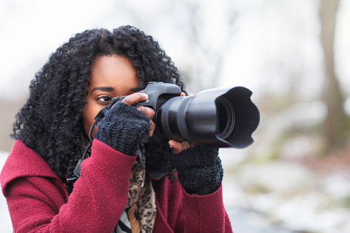 A woman outdoors with a digital SLR camera taking pictures on a winter day.