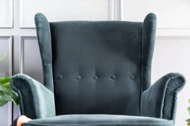 Photo of Close up high back green velvet armchair with gray painted wall in the background / interior concept / empty space for advertising