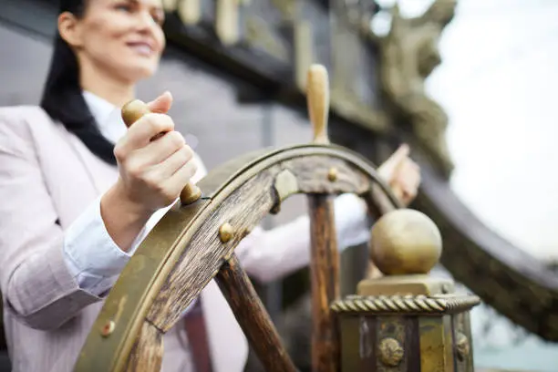 Hand of young successful businesswoman turning sailing wheel while leading large ship