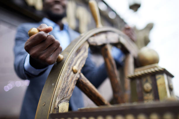 Leading ship Hand of African-american business leader holding by large wooden sailing wheel while turning it ships wheel name stock pictures, royalty-free photos & images