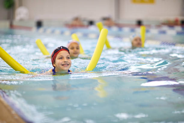 маленькая девочка с плавающей лапшой - swimming child swimming pool indoors стоковые фото и изображения