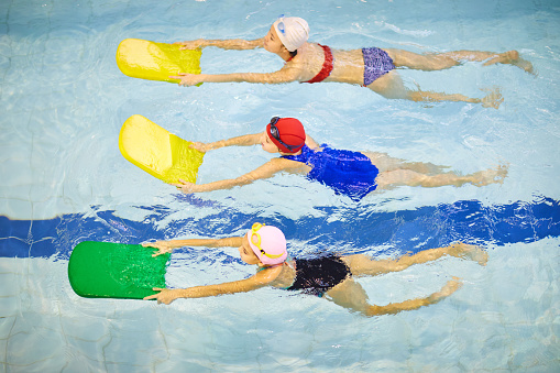 Group of little girls in swimwear swimming with kickboards in pool during swimming lesson
