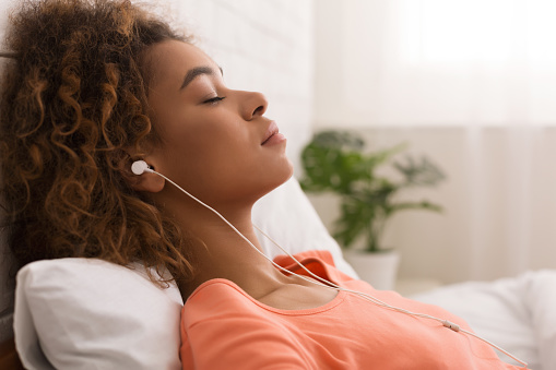 African-american woman listening calm music and relaxing, lying in bed