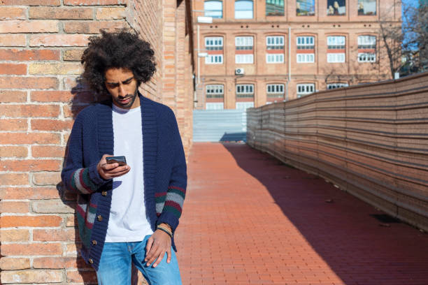 istock Young handsome African man using his smartphone with smile while leaning on a bricked wall outdoors in sunny day 1125926947