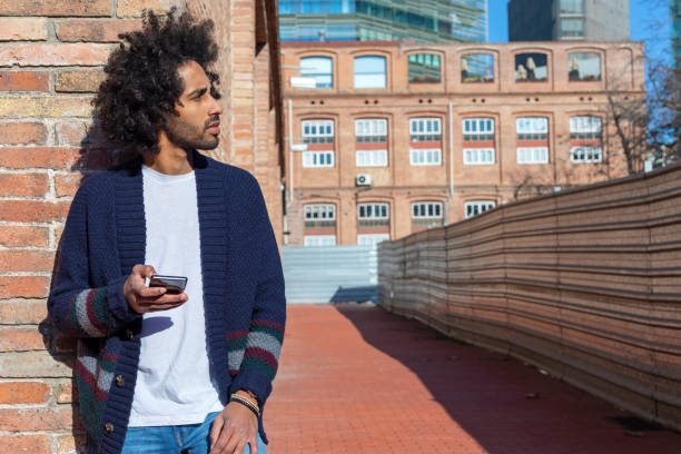 istock Young handsome African man using his smartphone with smile while leaning on a bricked wall outdoors in sunny day 1125926987