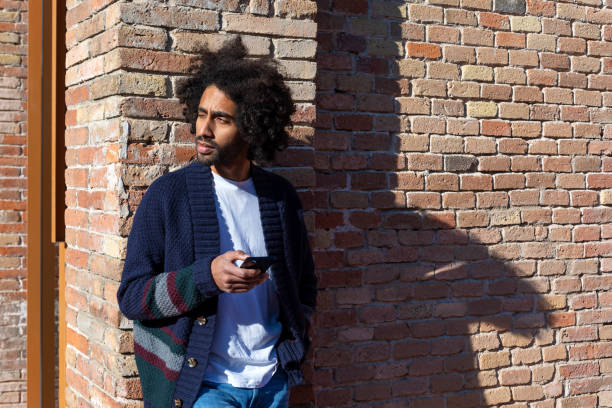 istock Young handsome African man using his smartphone with smile while leaning on a bricked wall outdoors in sunny day 1125927050
