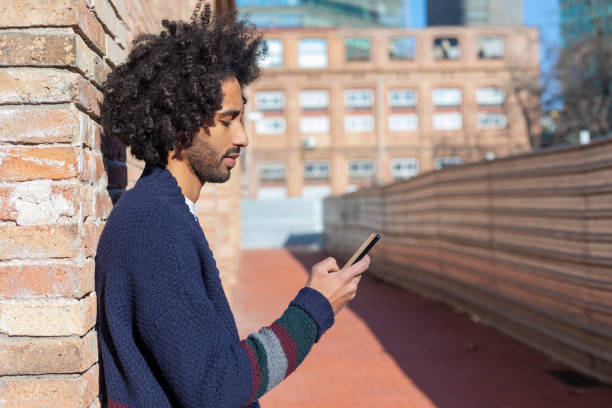 istock Young handsome African man using his smartphone with smile while leaning on a bricked wall outdoors in sunny day 1125927052