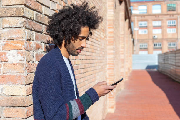 istock Young handsome African man using his smartphone with smile while leaning on a bricked wall outdoors in sunny day 1125927100