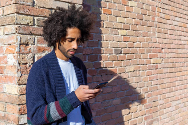istock Young handsome African man using his smartphone with smile while leaning on a bricked wall outdoors in sunny day 1125927175