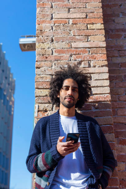 istock Young handsome African man using his smartphone with smile while leaning on a bricked wall outdoors in sunny day 1125927206