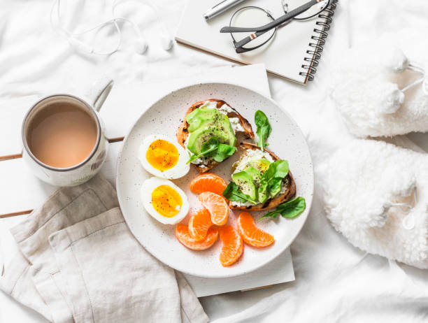 womens gemütliches frühstück im bett-stillleben - kaffee, avocado-sandwiches, gekochtes ei und mandarine auf einem hellen hintergrund, ansicht von oben. morgen-inspiration-plan - cheese plant stock-fotos und bilder