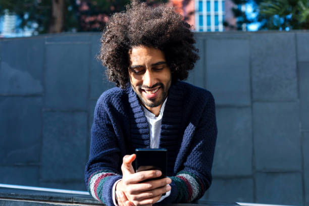 istock Young handsome African man using his smartphone with smile while leaning on a fence outdoors in sunny day 1125927639