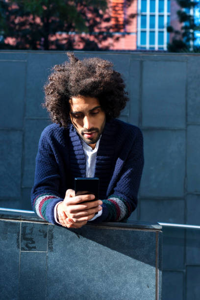 istock Young handsome African man using his smartphone with smile while leaning on a fence outdoors in sunny day 1125927827