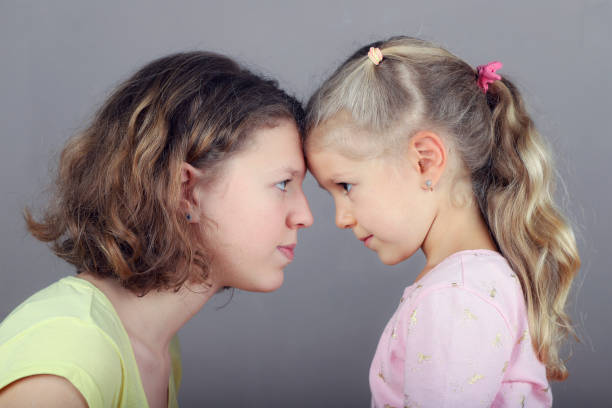 Two sisters stand opposite each other head to head, face to face, make eye contact. Two sisters stand opposite each other head to head, face to face, make eye contact. teenager couple child blond hair stock pictures, royalty-free photos & images