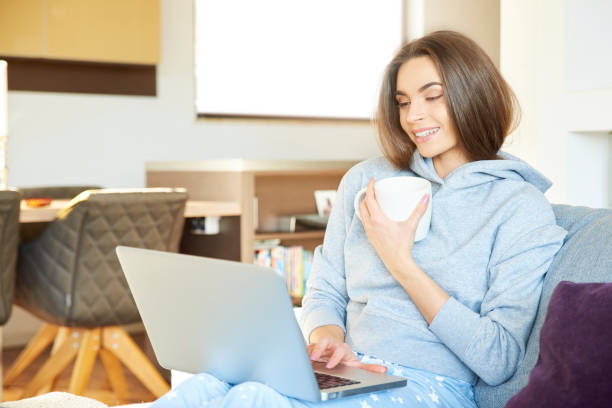 istock Young woman with her laptop sitting on sofa at home and drinking tea 1125941148